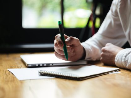 Cropped photo of mans hand holding green pen, while taking notes